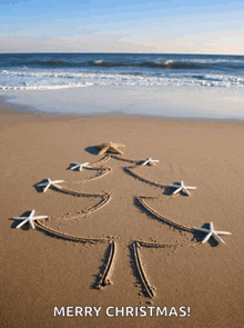 a merry christmas card with a christmas tree drawn in the sand on the beach