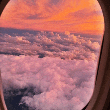 a view of clouds from an airplane window with a sunset in the background