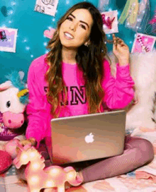 a woman in a pink sweater is sitting on a bed with an apple laptop .