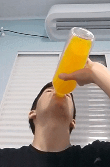 a man is drinking a bottle of orange juice in front of a window