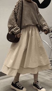 a woman wearing a striped sweater and a beige skirt