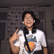 a young boy wearing headphones and glasses is giving a peace sign .