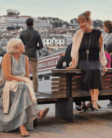 two women are sitting on a bench in front of a bridges cruise sign