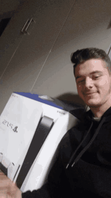 a man in a black hoodie is holding a ps5 in a box