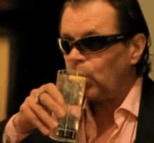 a man wearing sunglasses drinks from a glass