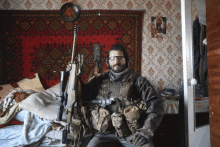 a man in a military uniform is holding a rifle in a bedroom