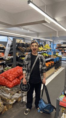 a man in a plaid shirt is standing in a grocery store holding a blue bag