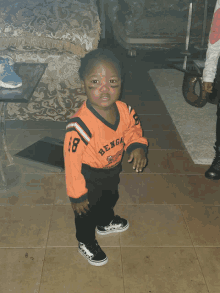 a little boy wearing a bengals jersey stands on a tiled floor