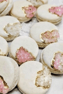 a close up of a bunch of macarons with pink crystals and gold foil .