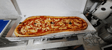 a very long pizza is sitting in a box on a stove top