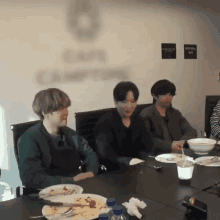 a group of young men are sitting around a table with plates of food