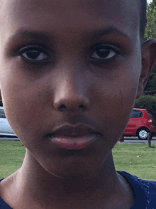 a young boy looks at the camera with a red car in the background