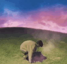 a man is kneeling down in a grassy field with a purple sky in the background .