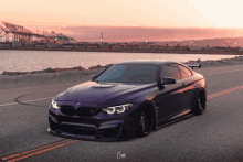 a purple bmw is parked on a road near a body of water