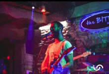 a man sings into a microphone while playing a guitar in front of a sign that says the bit