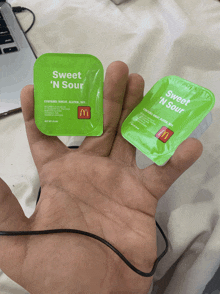 a hand holding two packets of sweet n sour sauce