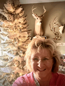 a woman is smiling in front of a christmas tree and a deer head