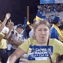 a woman wearing a yellow shirt with the word capriles radon on it is standing in front of a crowd of people .