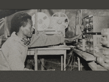 a black and white photo of a man sitting in front of a tape machine