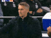 a man in a black jacket stands in front of a scoreboard that says ' manchester united ' on it