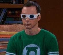 a man wearing 3d glasses and a green lantern shirt is sitting on a couch .