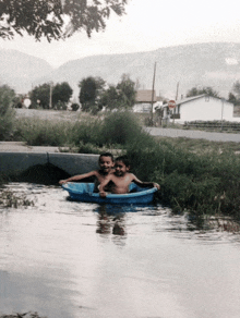 two young boys in a blue tub in a river with mountains in the background