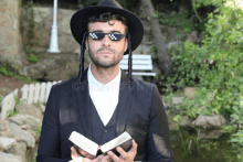 a man wearing a hat and sunglasses holds a bible