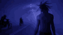 a man with dreadlocks is walking down a street in a dark tunnel with two people riding motorcycles in the background .