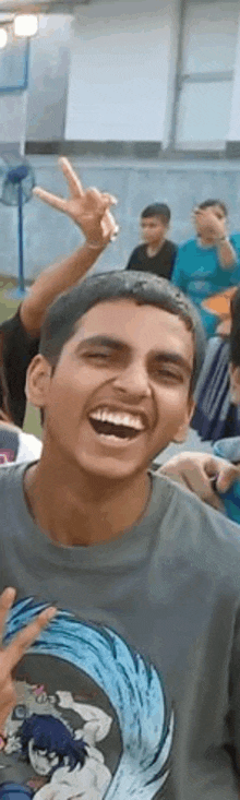 a young man is laughing and giving a peace sign while wearing a t-shirt .