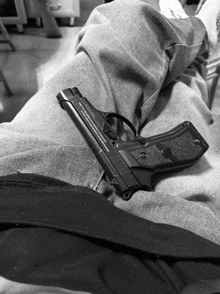 a black and white photo of a person laying on a bed with a gun on their lap