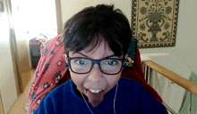 a young boy wearing glasses and ear buds sticks out his tongue