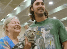 a man in a green shirt holds a cat next to a woman who is smiling