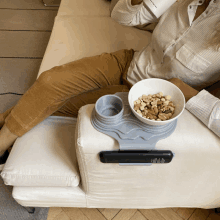 a woman sits on a couch with a bowl of cereal and a remote