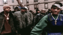 a group of men are standing in front of a building and one of them is wearing a blue vest .