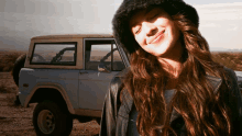 a woman stands in front of a blue jeep