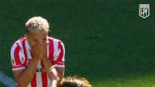 a soccer player wearing a red and white striped jersey with the number 15 on it is kneeling on the field .