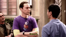 a man in a purple shirt is talking to another man while another man looks on .