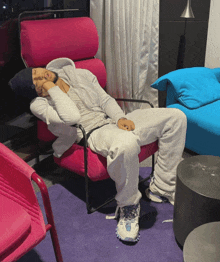 a man sleeping in a pink chair with a blue couch in the background