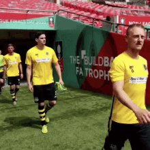 a group of soccer players are walking out of a stadium that has a sign that says the buildba fa trophy