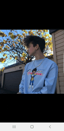 a young man is wearing a light blue sweatshirt with a picture of vegeta on it .