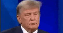 donald trump is wearing a suit and tie and making a funny face on a blue background .