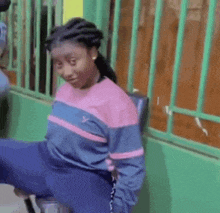 a woman in a pink and blue sweater is sitting on a chair in front of a green wall .