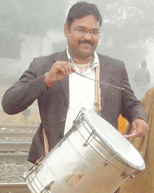 a man in a suit is holding a drum and a stick