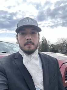 a man wearing a hat with a compass on it stands in front of a car