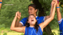 a group of female athletes in blue uniforms are raising their arms in the air in front of a tree ..