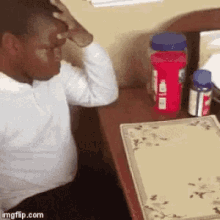 a man is sitting at a desk with his hand on his head and bottles of medicine on the table .