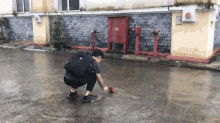 a man squatting down in front of a building with a red box on the side that says ' hydrant ' on it