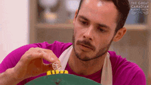 a man in a pink shirt is decorating a cake with the words the great canadian baking show behind him