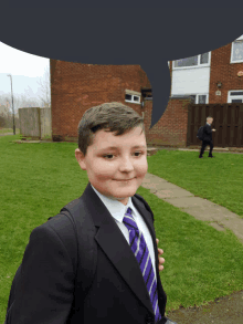 a boy in a suit and tie stands in front of a brick house