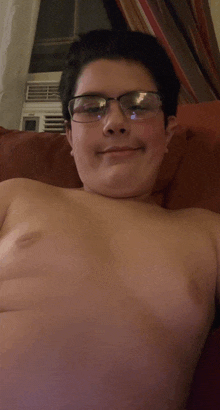 a shirtless boy wearing glasses is smiling